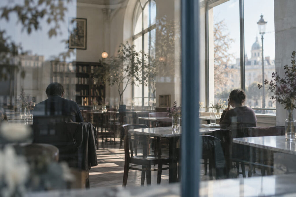 Interior luminoso de un café visto a través de un cristal, con dos personas sentadas a cierta distancia